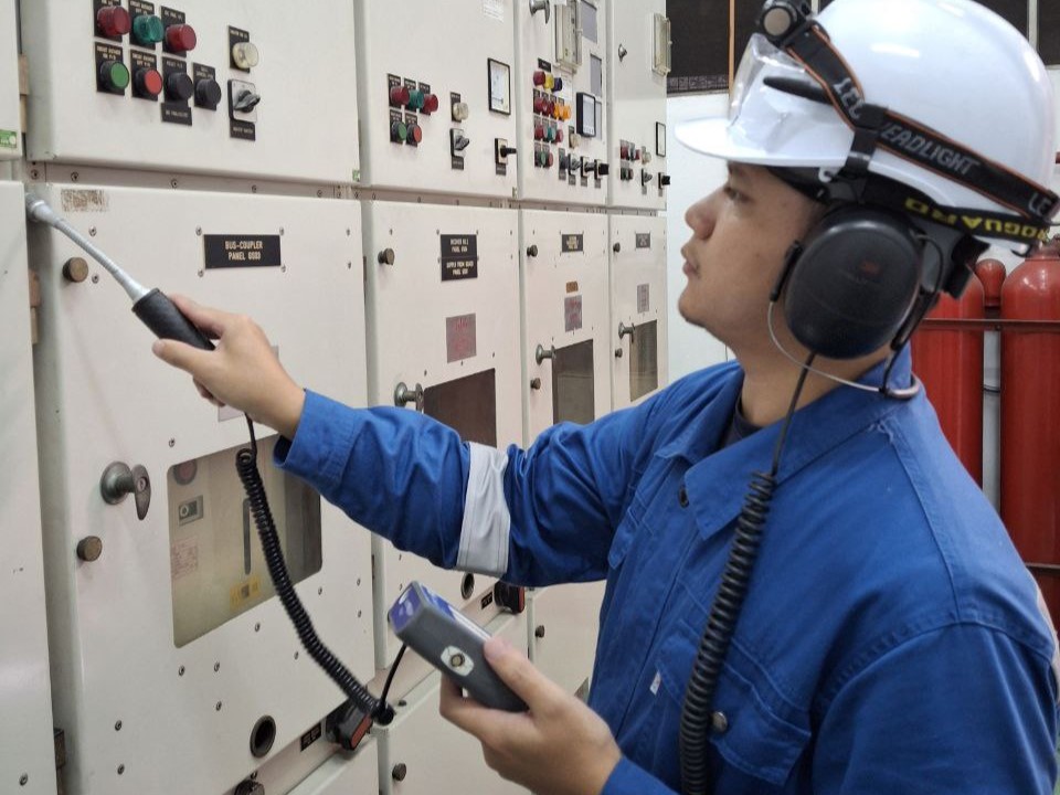 A technician wearing headphones using a flexible airborne ultrasound probe along closed switchgear panel joints